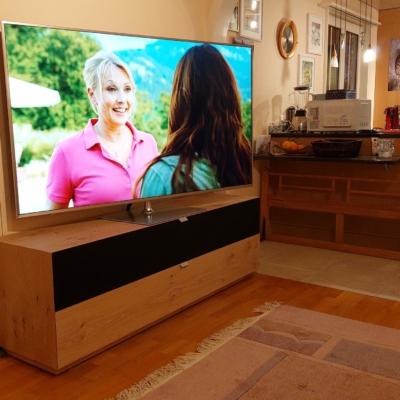 Schlichte elegante SwissHD Lösung; TV auf Drehfuss, Audio System unter der Stoffabdeckung sauber versorgt.